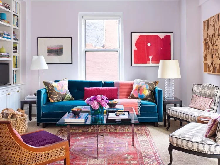 Small apartment living room with blue velvet sofa, patterned chairs, and colorful art.